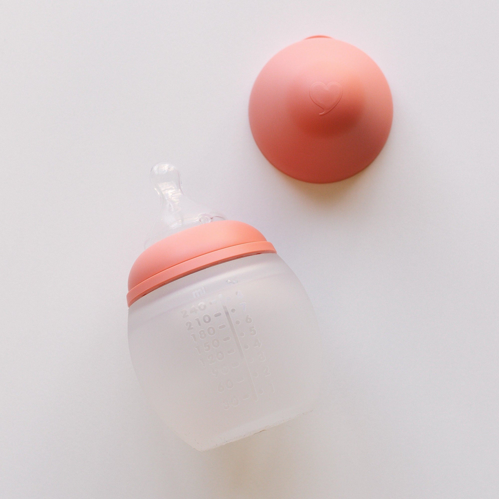 A BibRond summer coral baby bottle by Elhée France laying on a white surface.