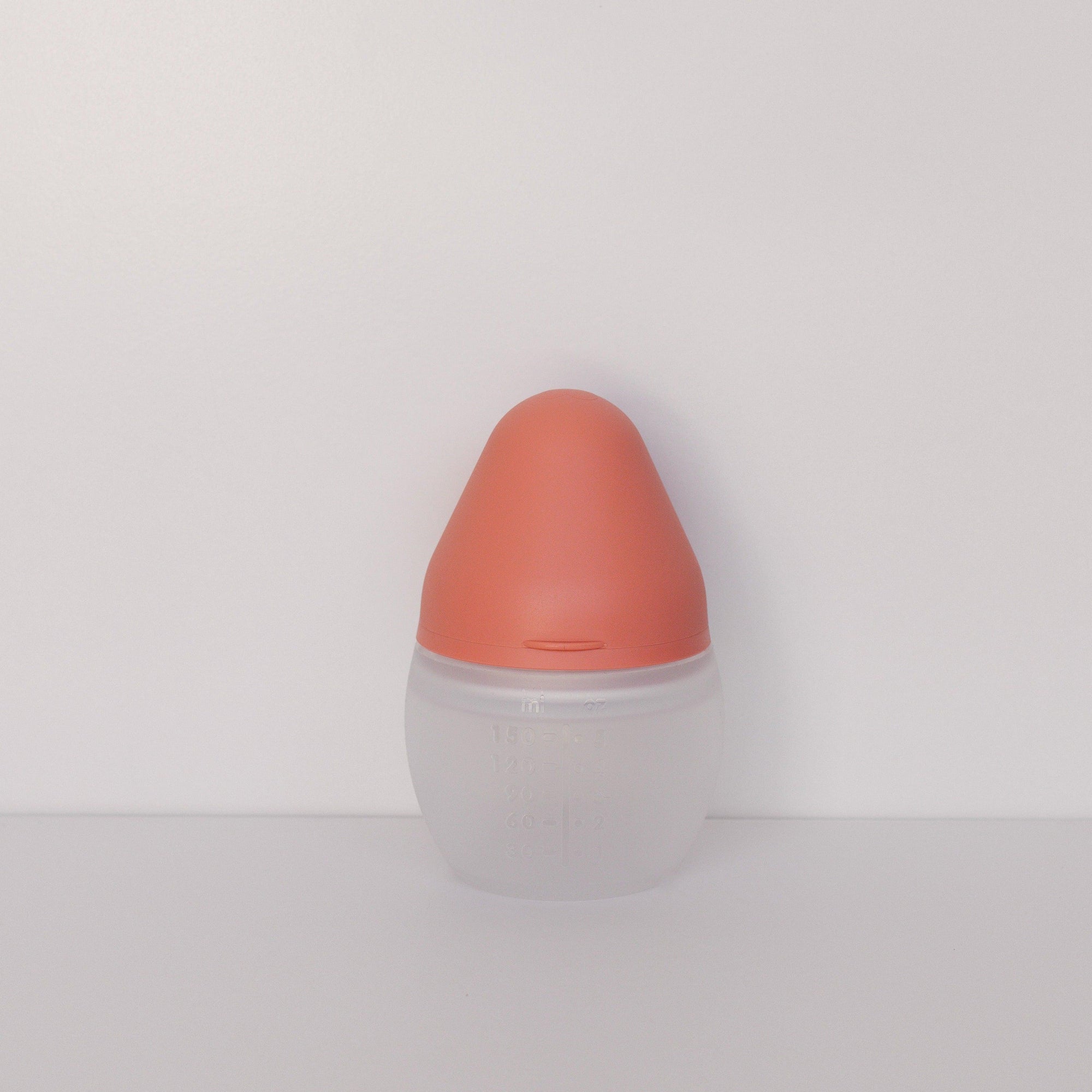 A BibRond summer coral baby bottle by Elhée France standing on a white surface.