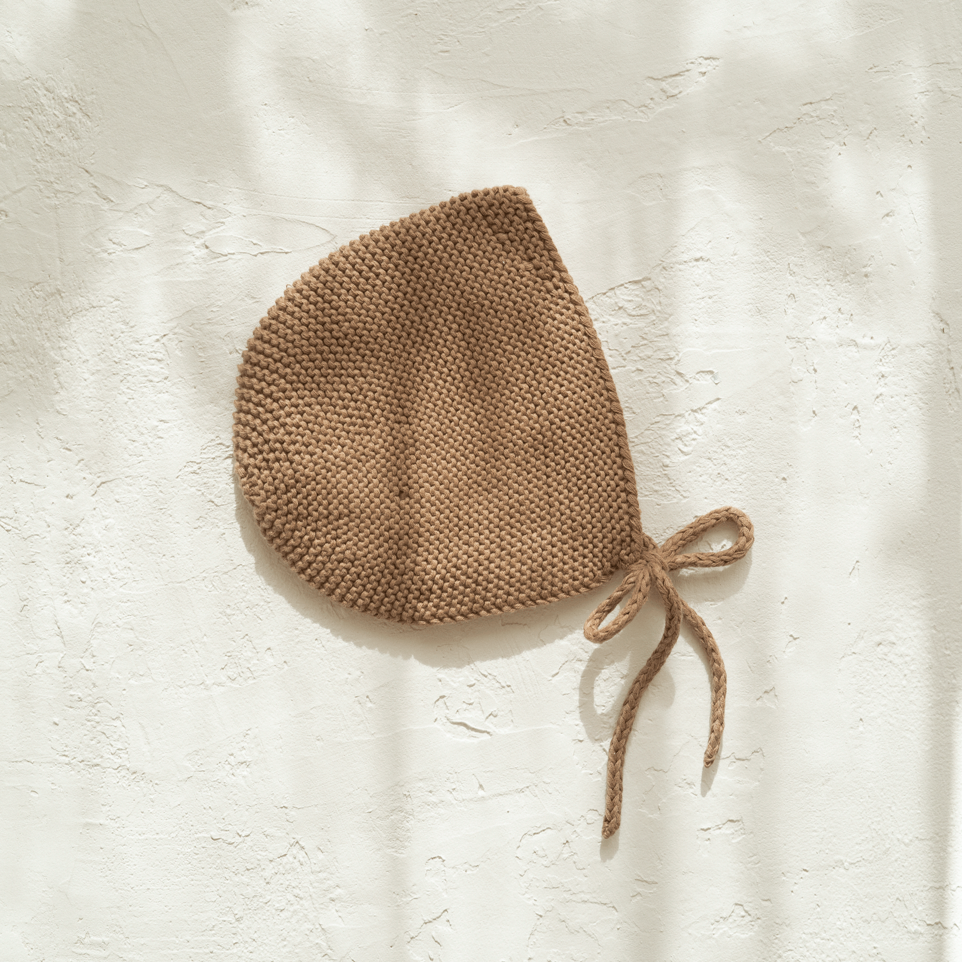 A Illoura baby bonnet | chocolate hanging on a wall.