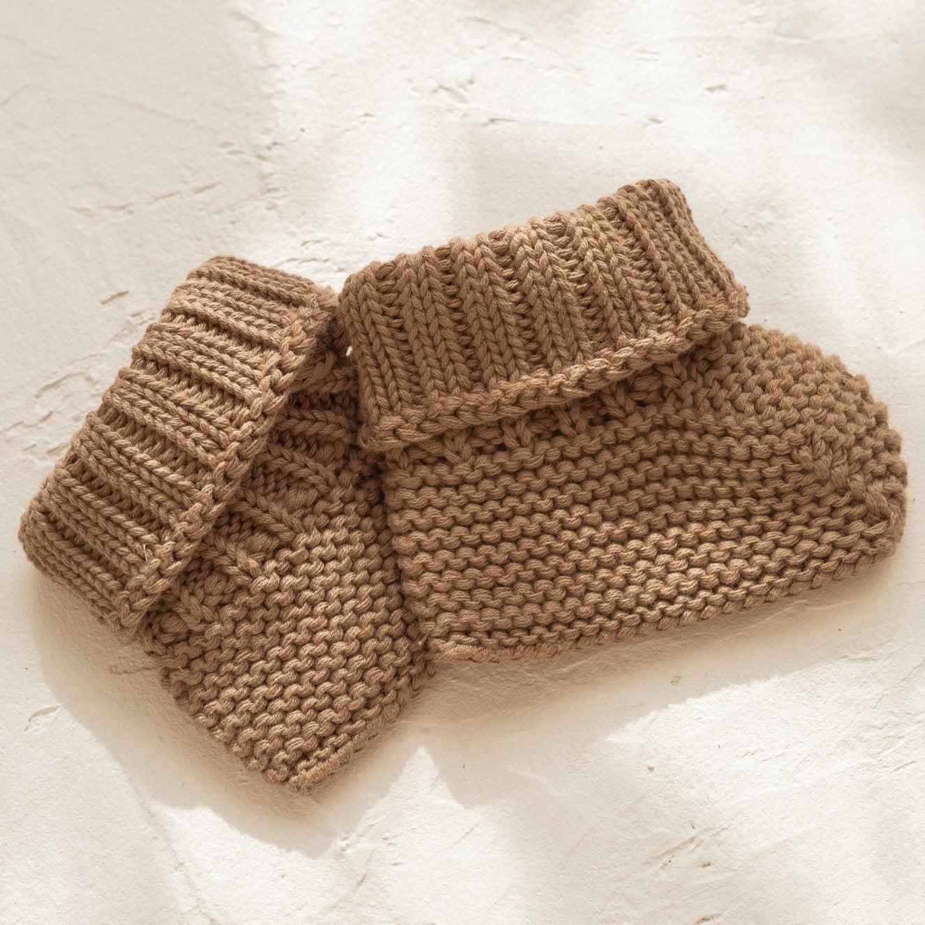 A pair of Illoura baby booties in chocolate made from organic cotton on a white surface.