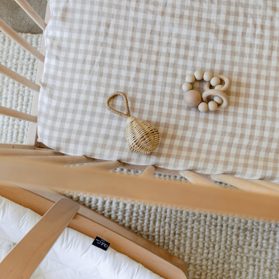 A baby's crib with a wooden toy on it, featuring Warren Hill French Linen fitted cot sheets and a neutral nursery.