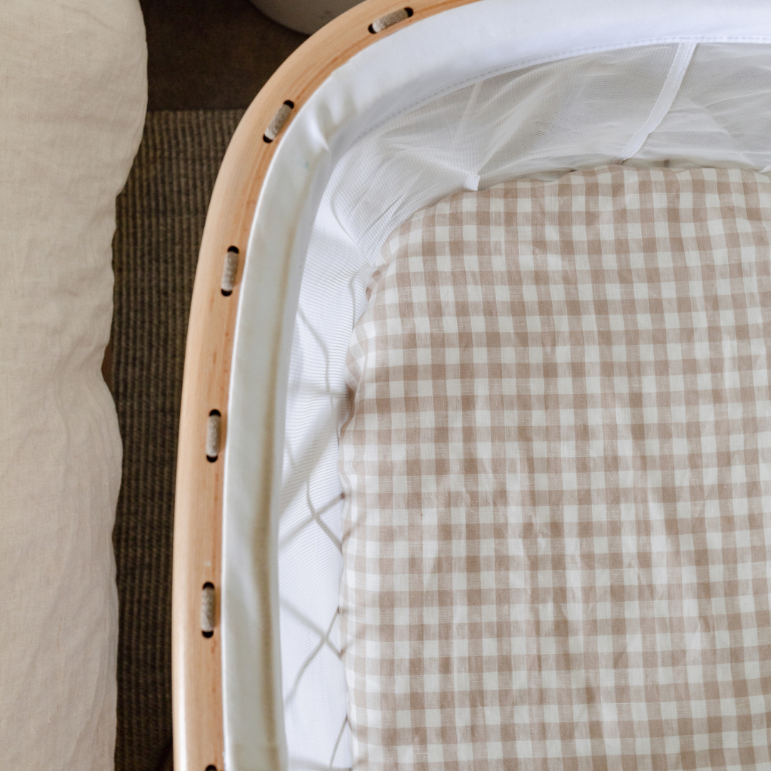 A baby crib with a French linen fitted bassinet sheet in beige gingham, perfect for a neutral nursery by Warren Hill.