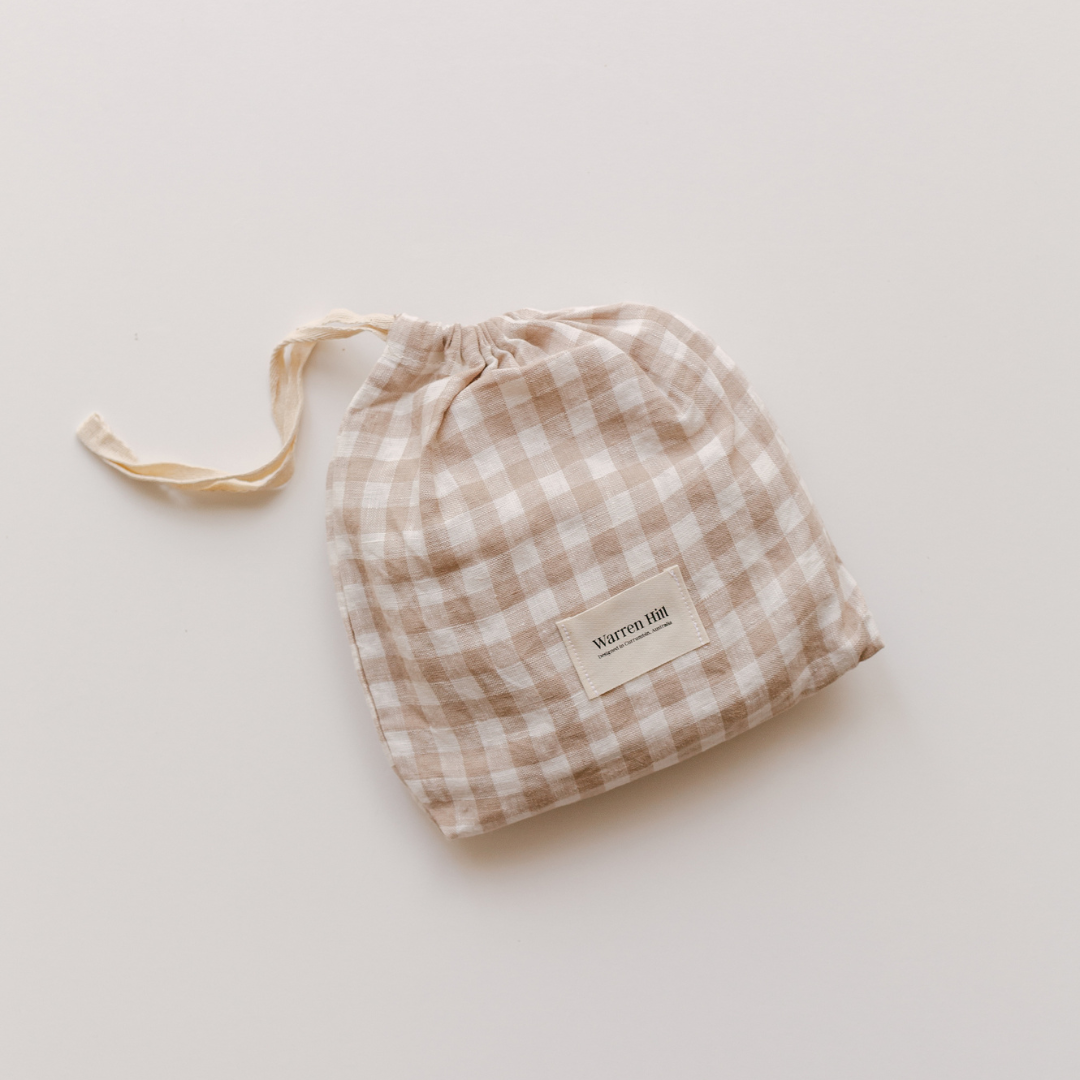 A Warren Hill french linen fitted bassinet sheet in beige gingham, on a white surface, suitable for neutral nursery decoration.