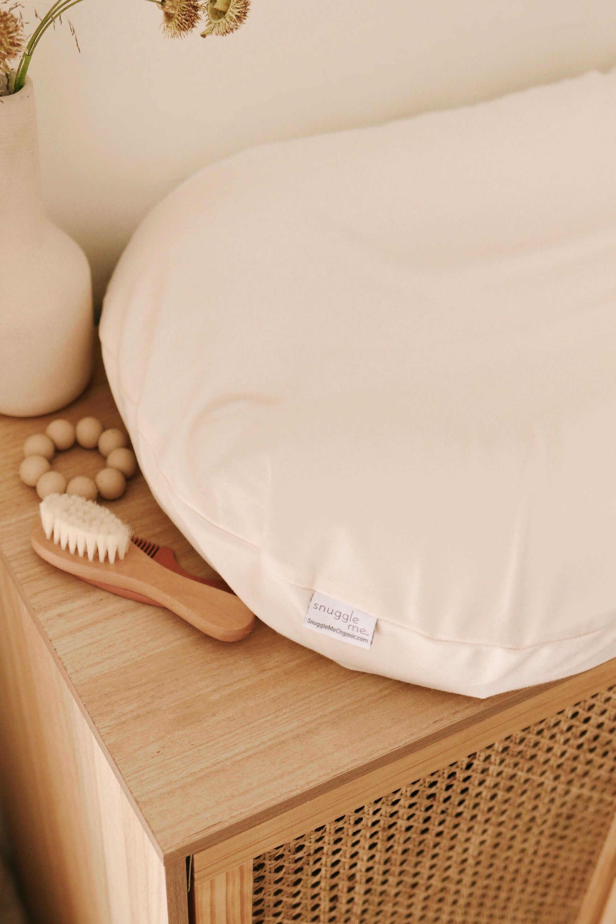A Snuggle Me Lounger Cover in Natural with a baby changing pad on it. The product is sturdy and made of high-quality wood, providing a reliable and stylish storage solution for your baby's essentials. The spacious drawers